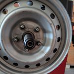 A silver steel car wheel rim mounted on a red wheel balancing machine